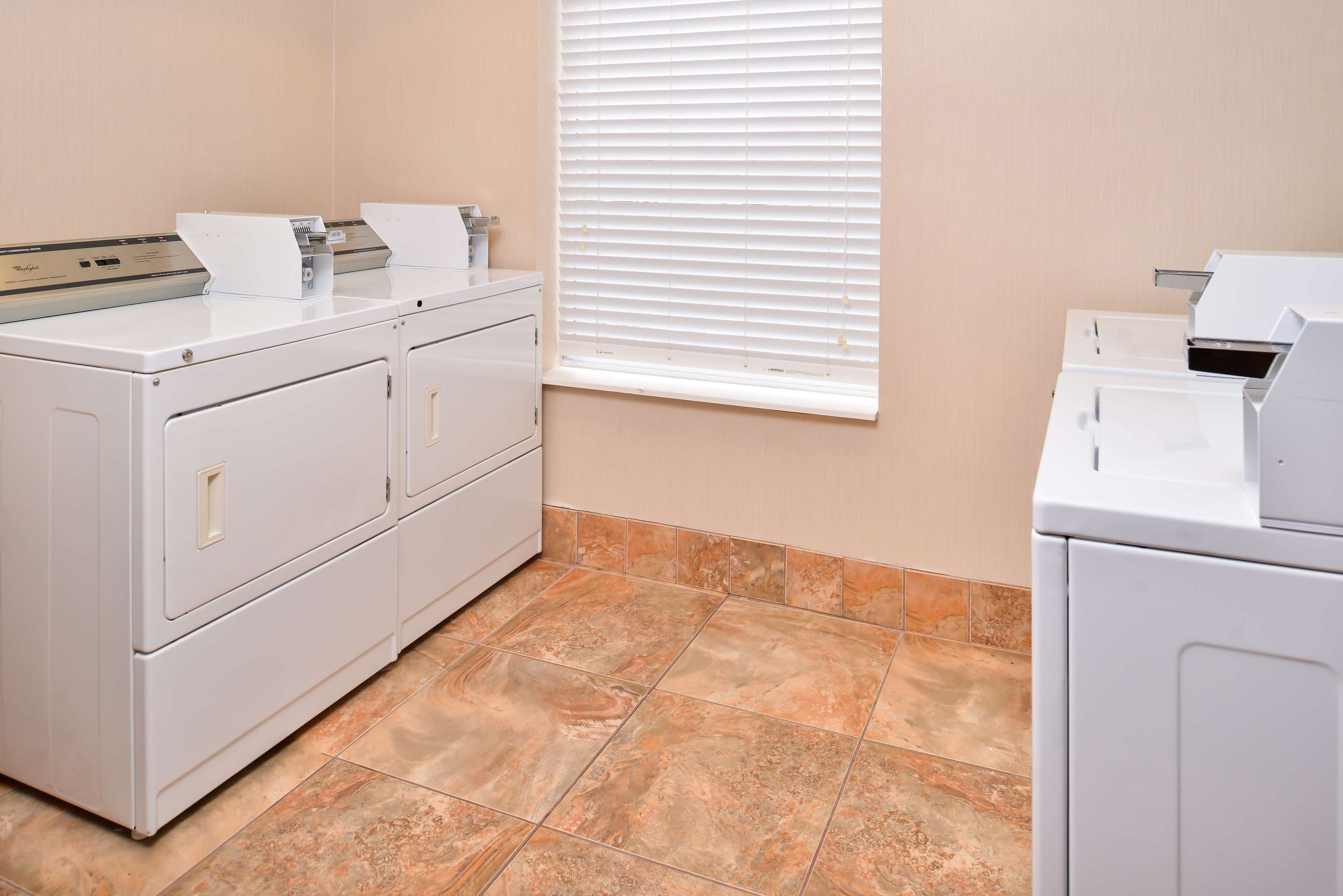 A laundry room with a front-loading washer and dryer, a utility sink, and a window with blinds.