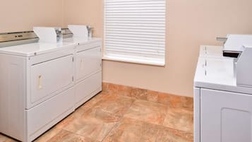 A laundry room with a front-loading washer and dryer, a utility sink, and a window with blinds.