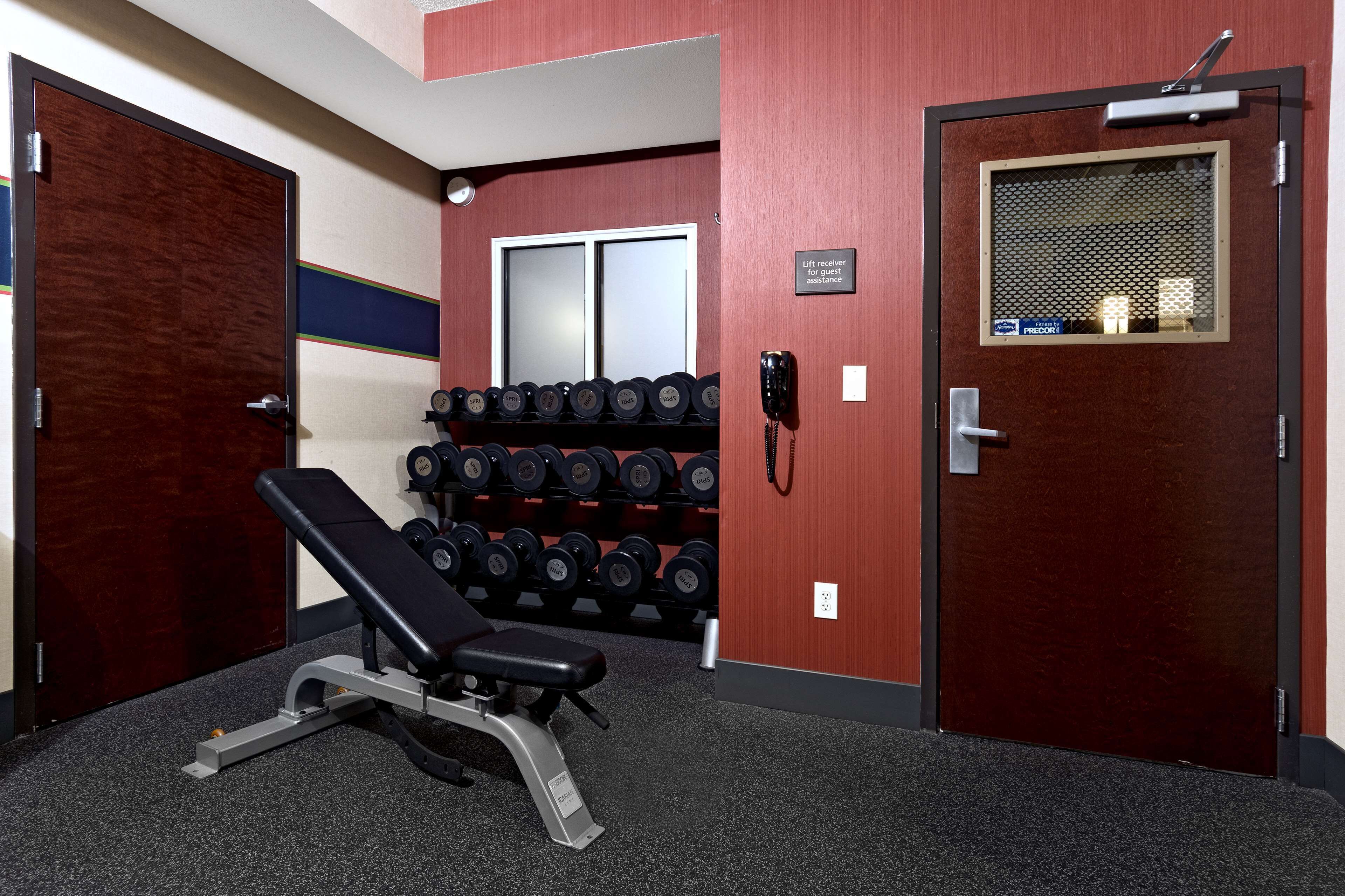 A gym with a bench press, dumbbells, and a phone on the wall.