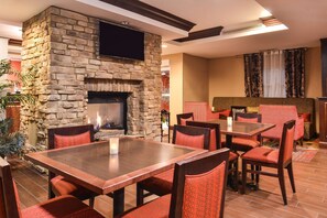 A dining area with a stone fireplace, wooden tables, and red upholstered chairs. - Hampton Inn Statesville (Statesville)