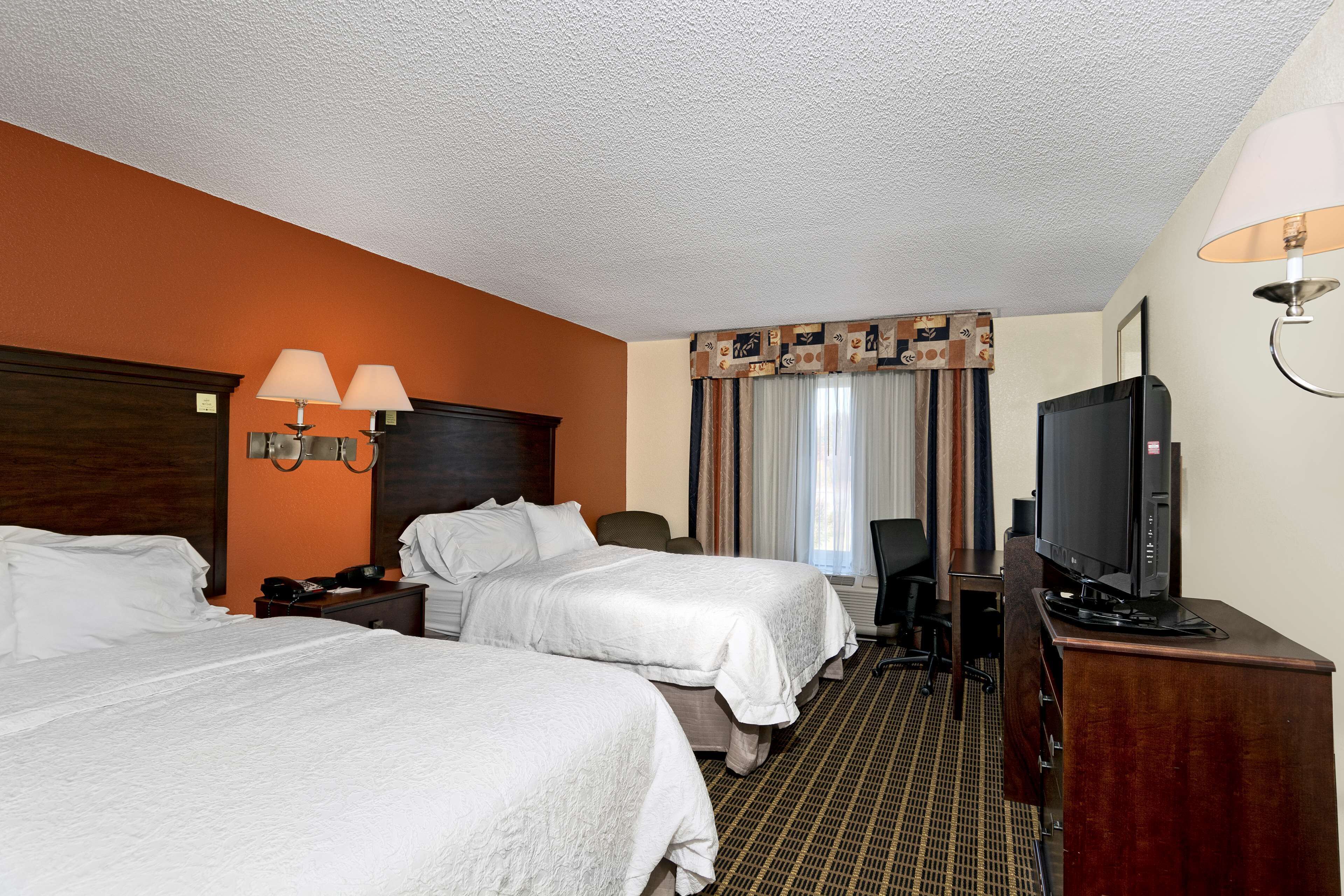 A hotel room with two beds, a desk with a television, and a lamp.
