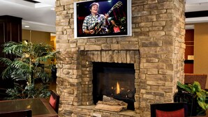 A stone fireplace with a television mounted above it, a dining area with chairs, and a large potted plant.