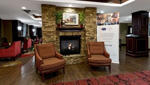 A lobby with a stone fireplace, two armchairs, a red carpet, and a banner.