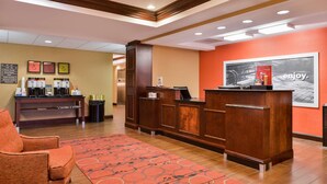 A hotel reception area with a wooden reception desk, a red carpet, and a coffee station.