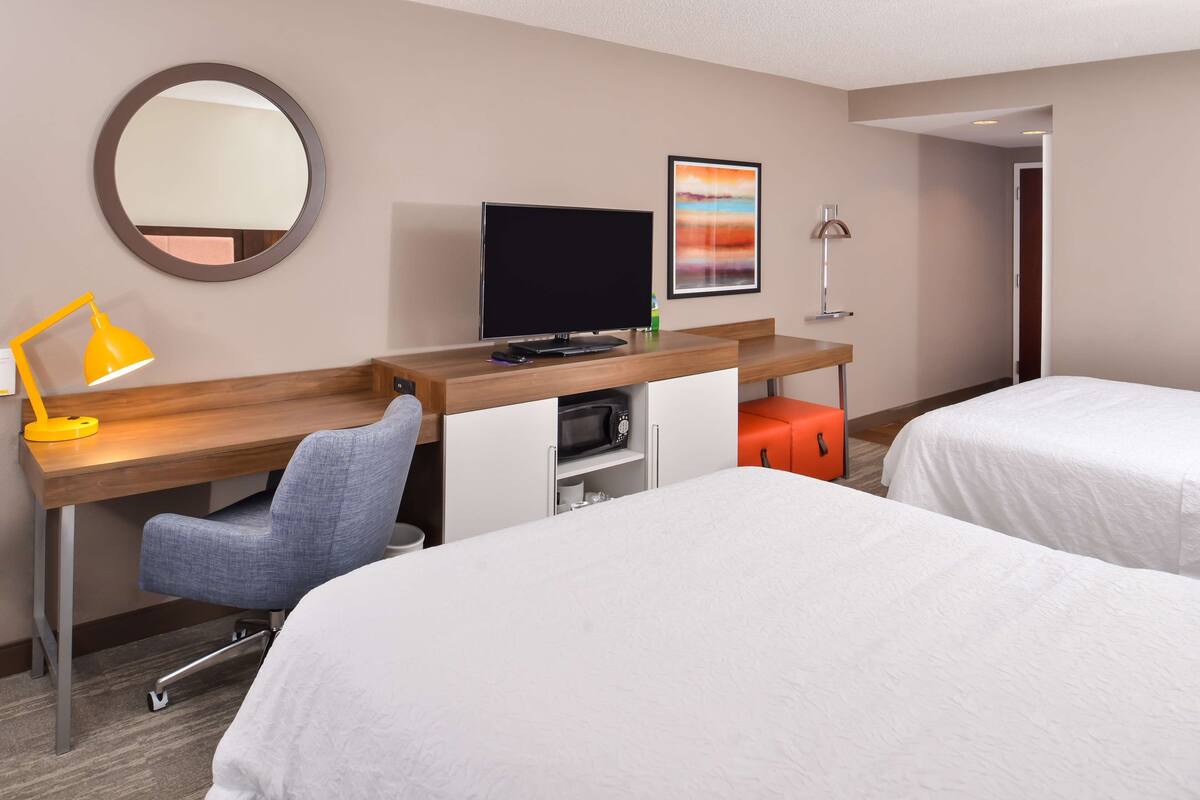 A hotel room with a desk, a chair, a TV, a bed, and a bathroom.