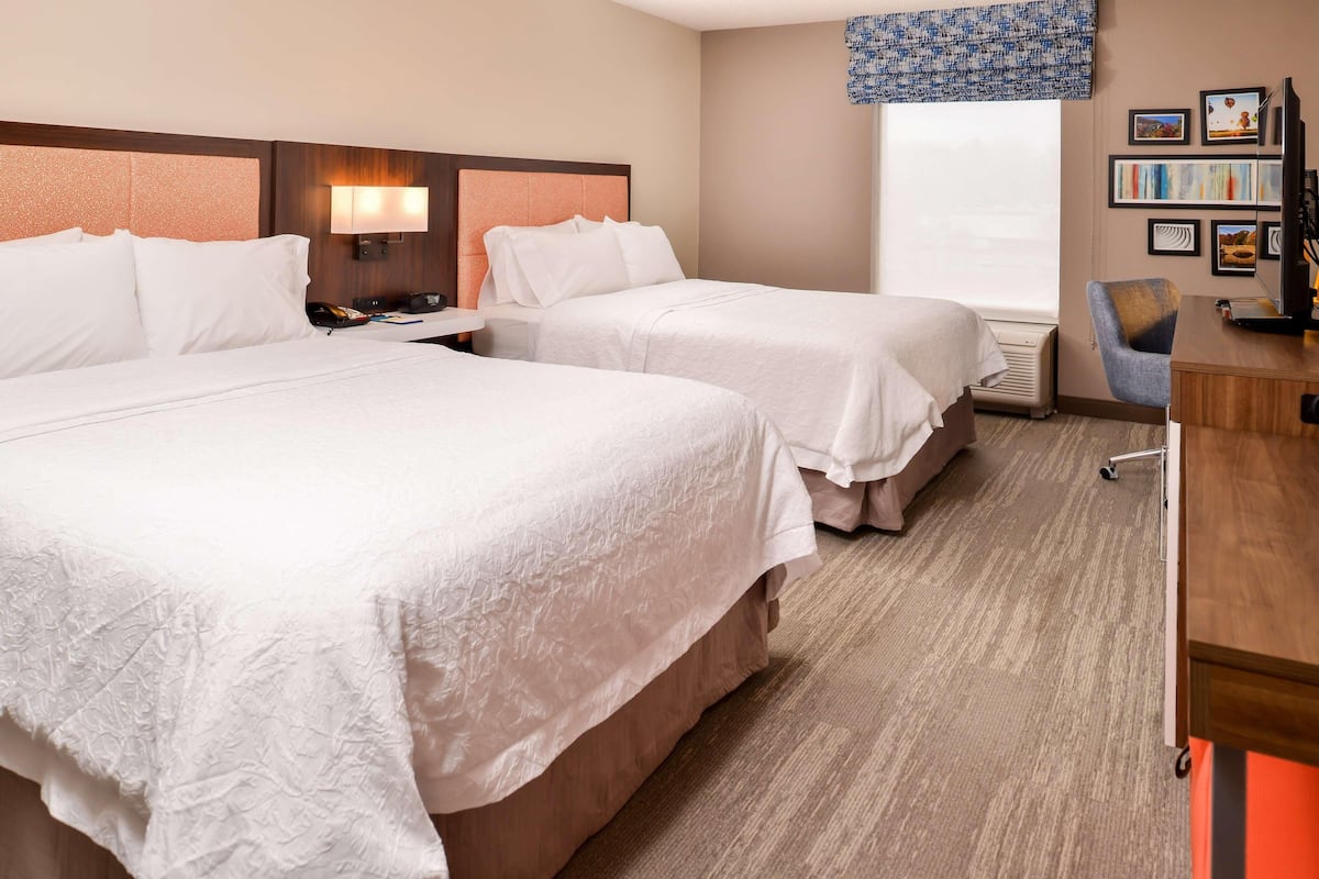 A hotel room with two beds, a desk, a chair, a TV, and a window with a view.
