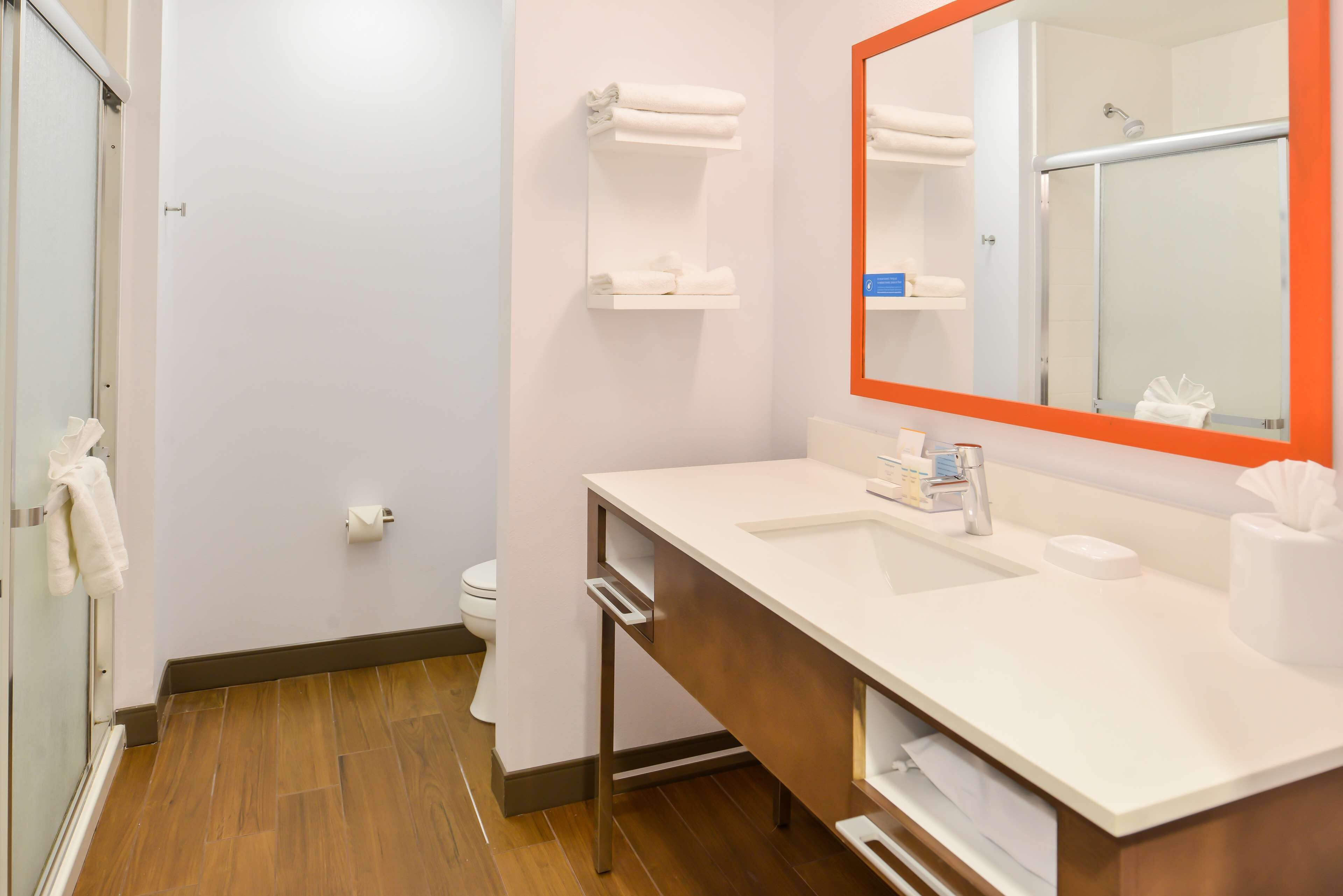 Un baño moderno con suelo de madera, lavabo blanco y un espejo grande de marco naranja.