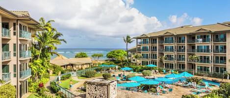 A resort with multiple buildings, a pool area with umbrellas, and a view of the ocean.