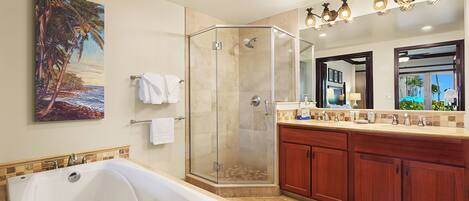 A modern bathroom with a large bathtub, a glass-enclosed shower, wooden cabinets, and a painting of a beach scene.