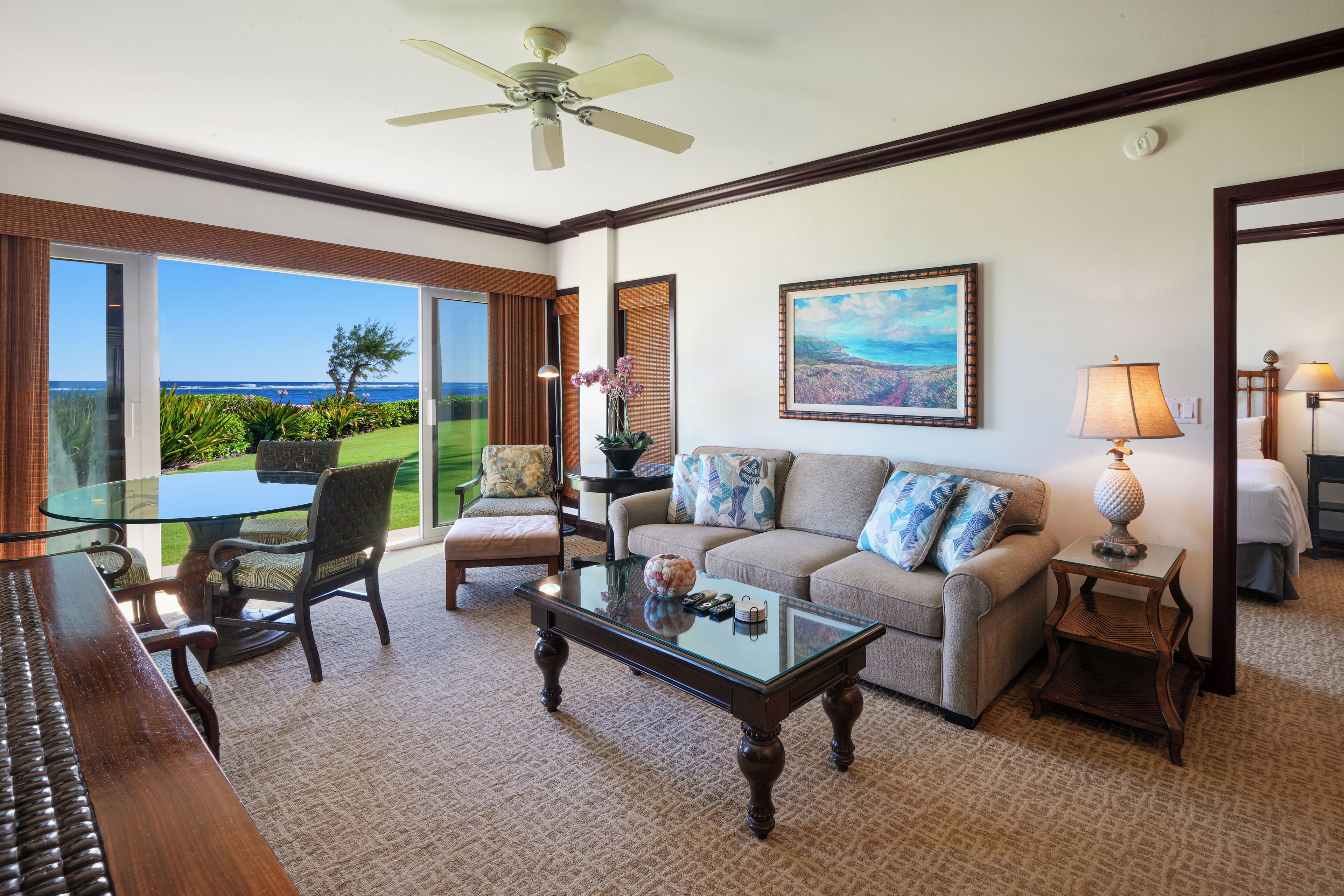 A spacious living room with a glass coffee table, a sofa with patterned cushions, a dining table with chairs, and a view of the ocean.