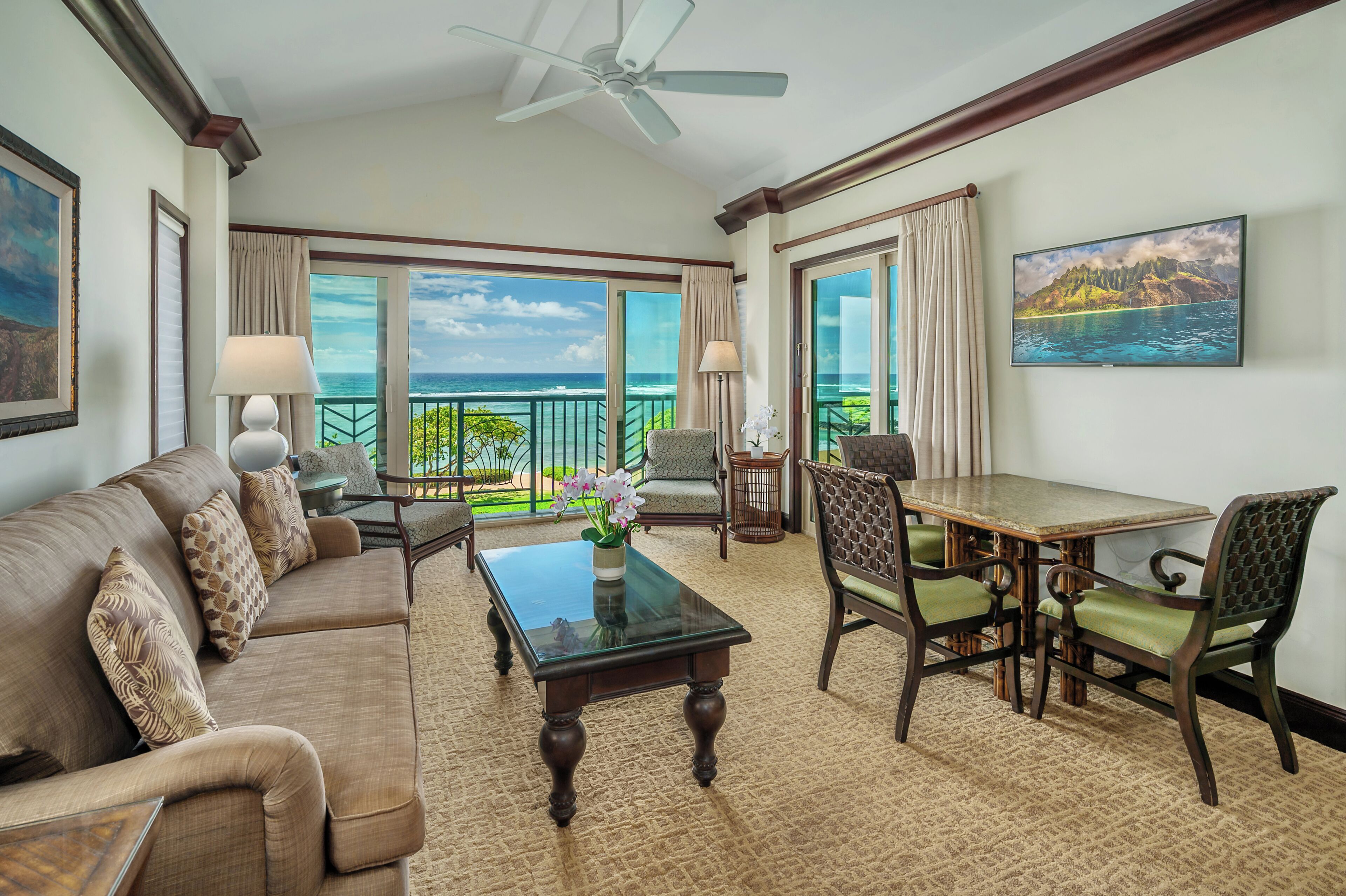A spacious living room with a balcony overlooking the ocean, furnished with a sofa, chairs, a coffee table, and a dining table.