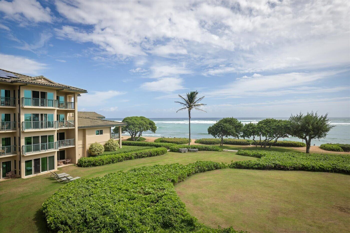 A multi-story hotel with balconies, a well-maintained lawn, and a view of the ocean.