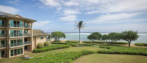 A multi-story hotel with balconies, a well-maintained lawn, and a view of the ocean.