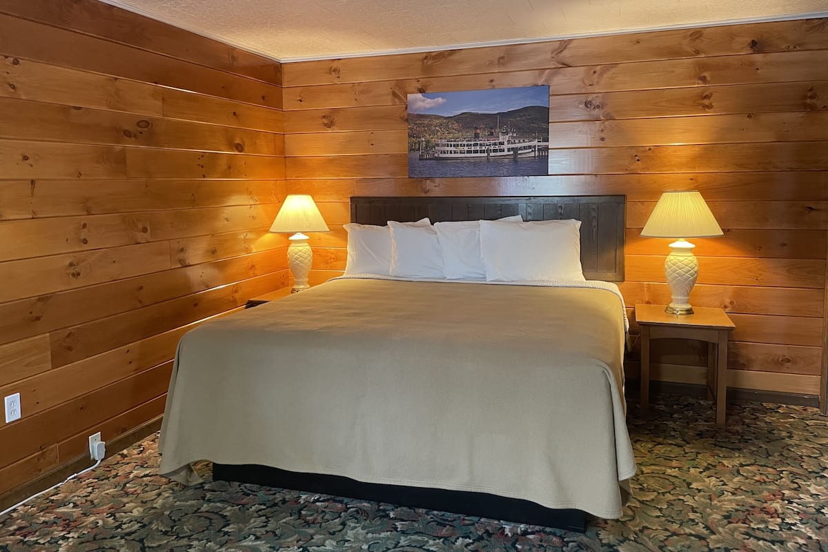A wooden-paneled room with a bed, two bedside lamps, and a framed picture on the wall.