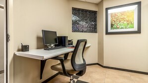 A modern office space with a desk, computer, and office chair. There is a framed picture on the wall and a window with a view of trees.