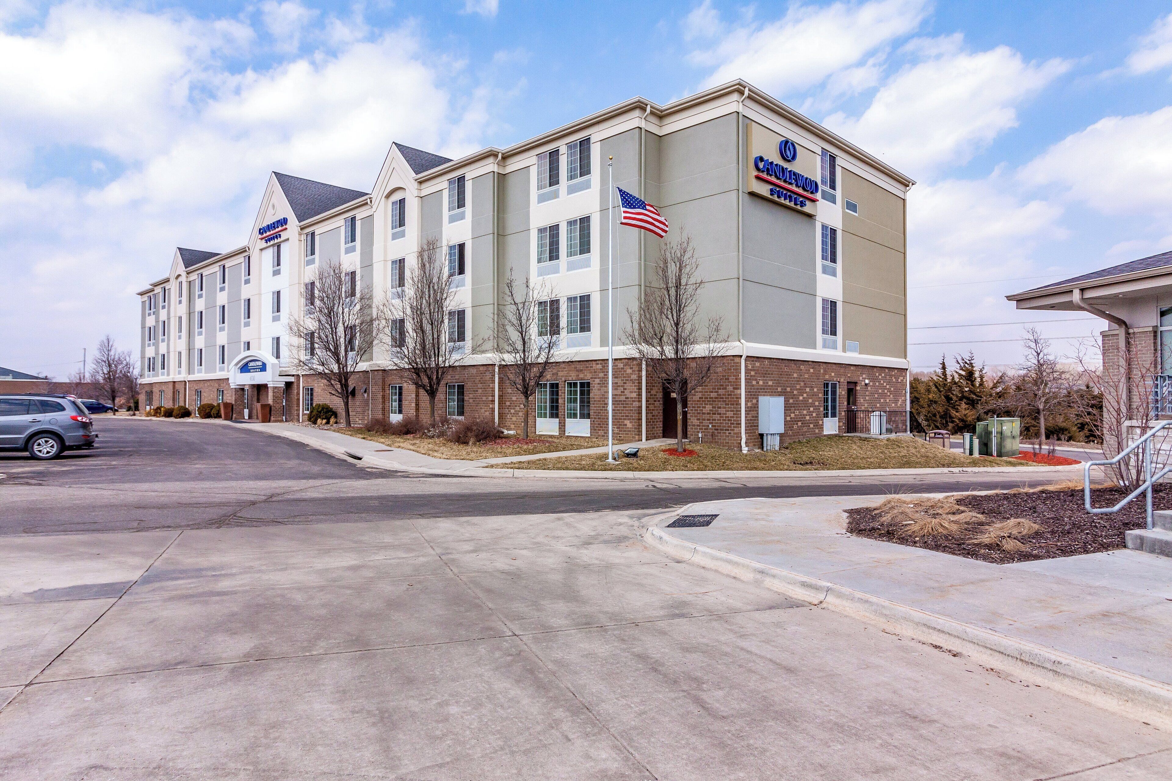 A multi-story hotel with a flat roof, a flag, and a parking lot.