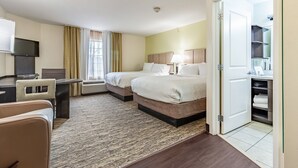 A hotel room with two beds, a desk, a TV, and a bathroom visible through an open door.