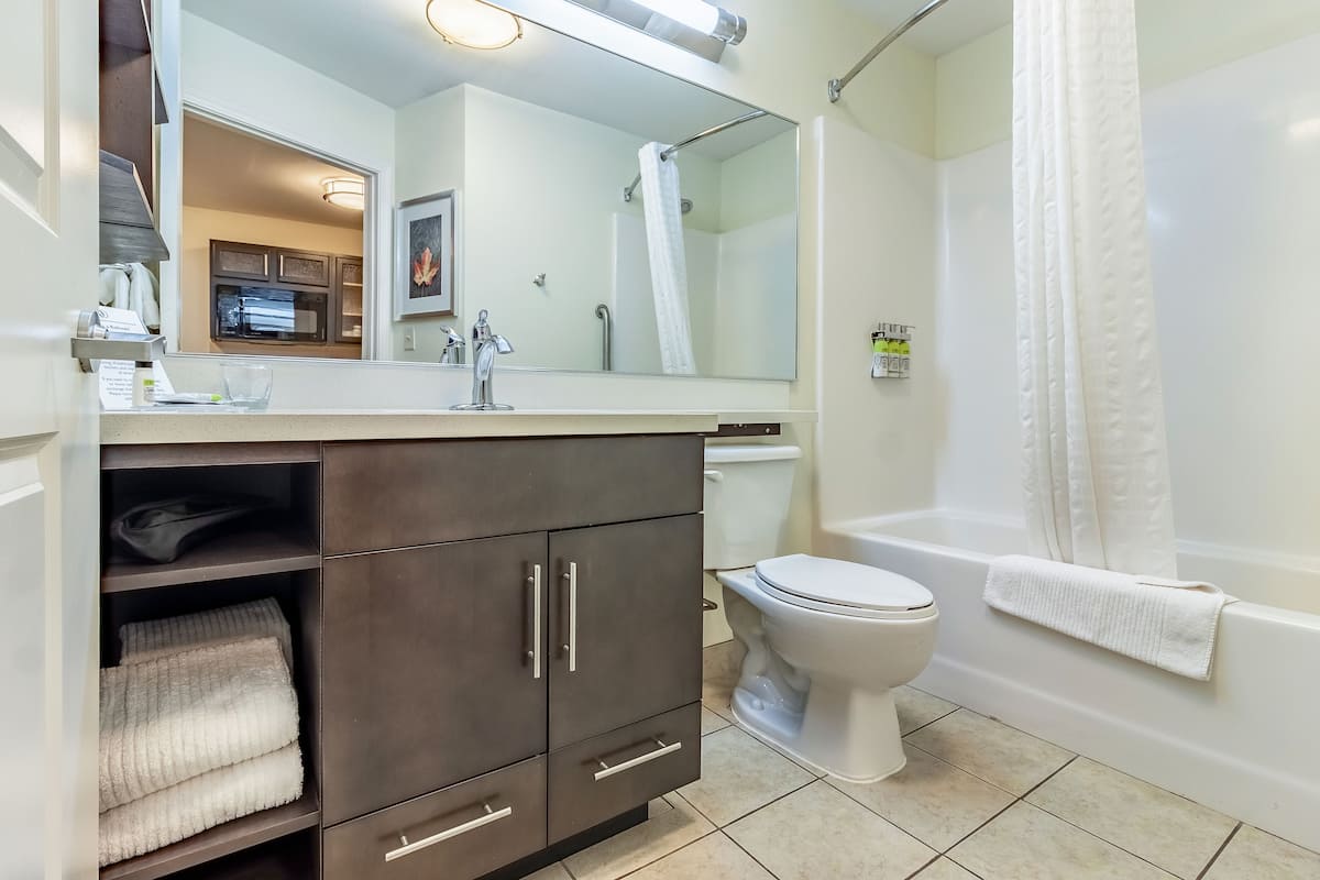 A modern bathroom with a large mirror, dark wooden cabinets, a white toilet, and a bathtub.