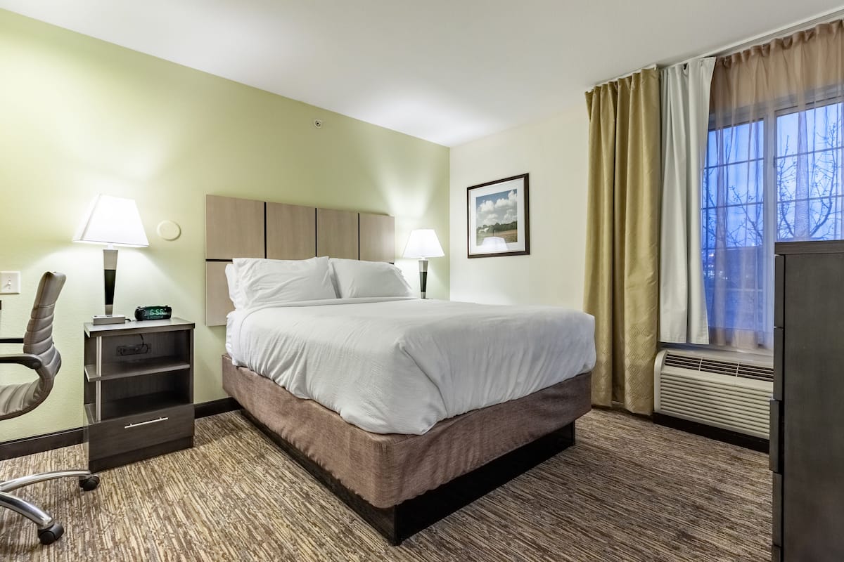 A hotel room with a bed, bedside lamps, a desk with a chair, a picture on the wall, and a window with curtains.