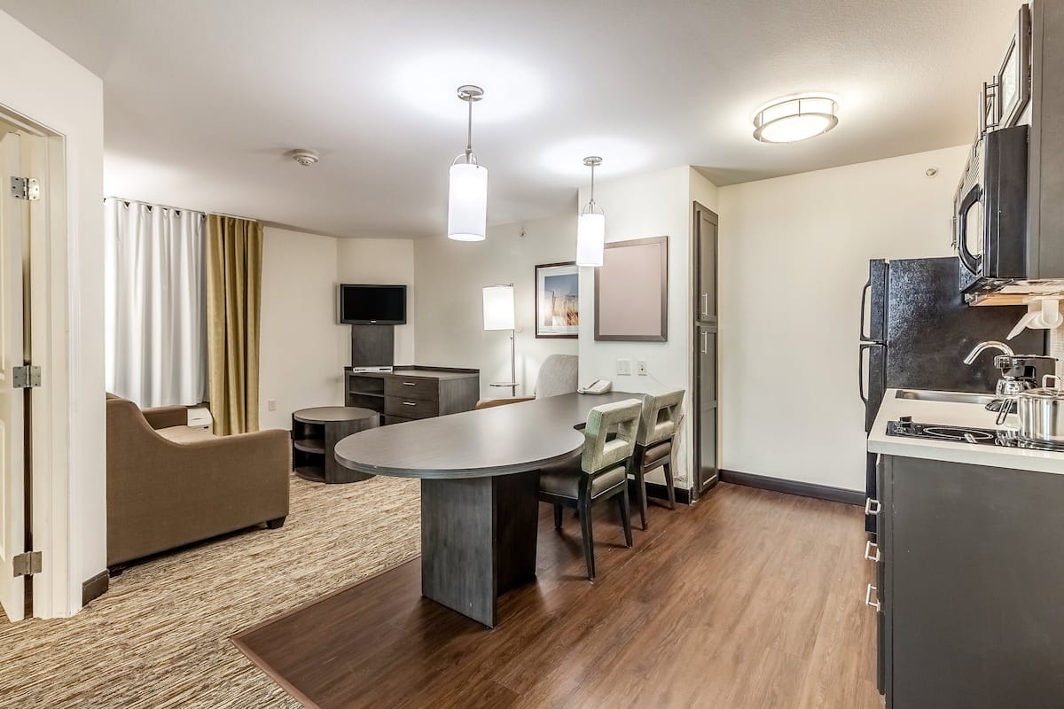 A modern living room with a dining table, sofa, and kitchen area including a refrigerator and microwave.