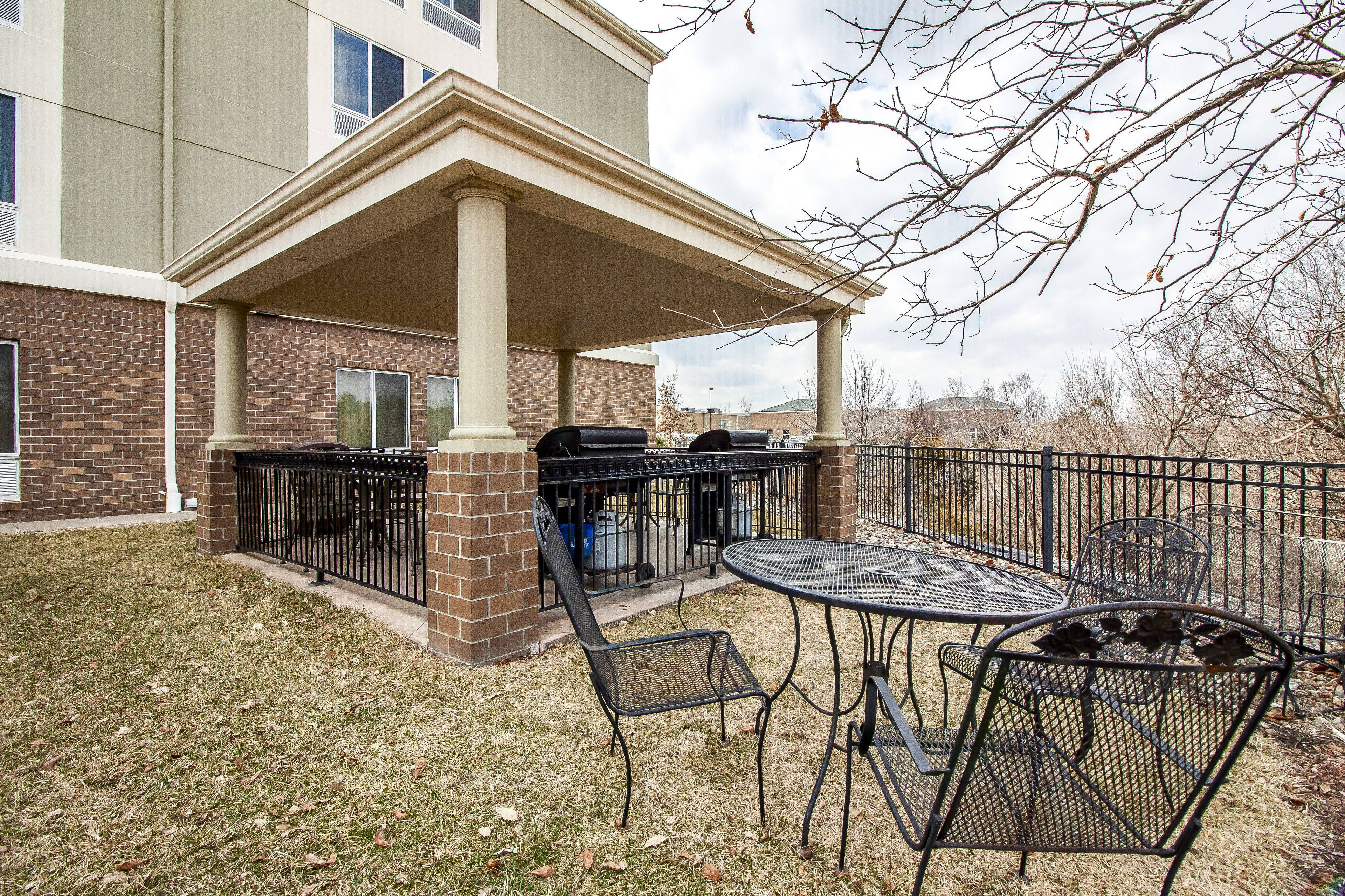 An outdoor patio with a covered seating area, a grill, and a trash can.