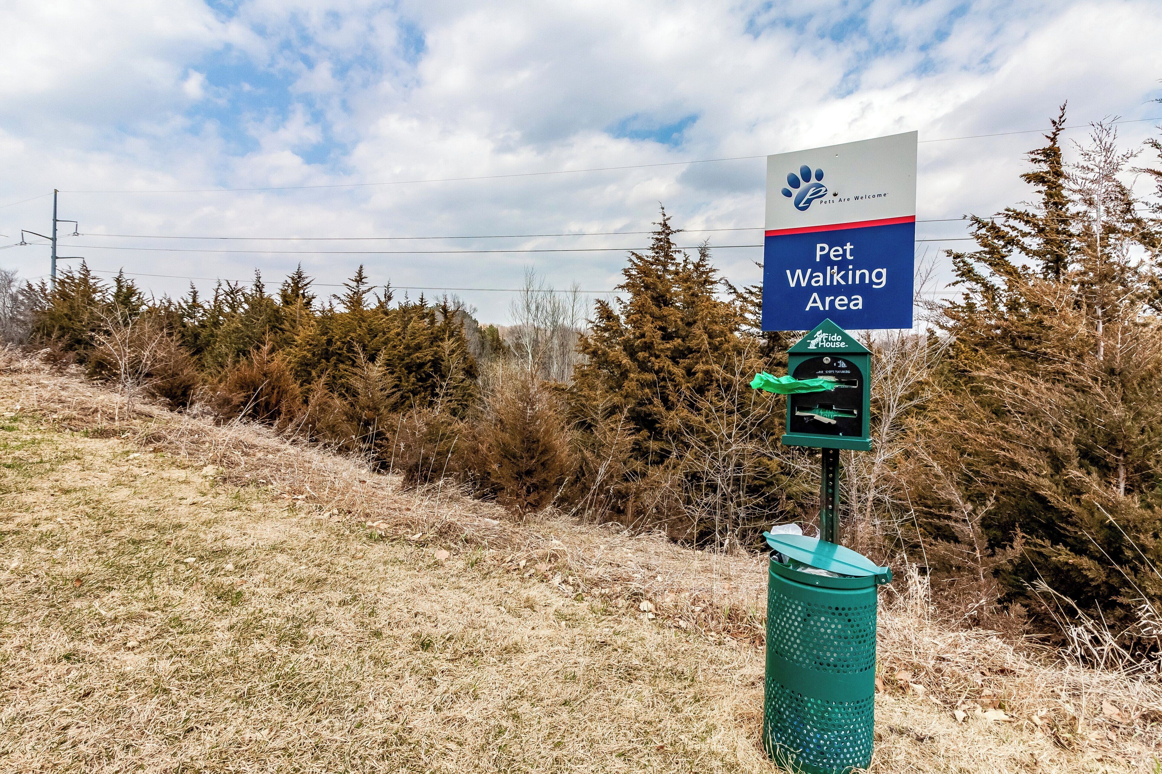 A sign indicating a pet walking area with a paw print logo and a green trash can.