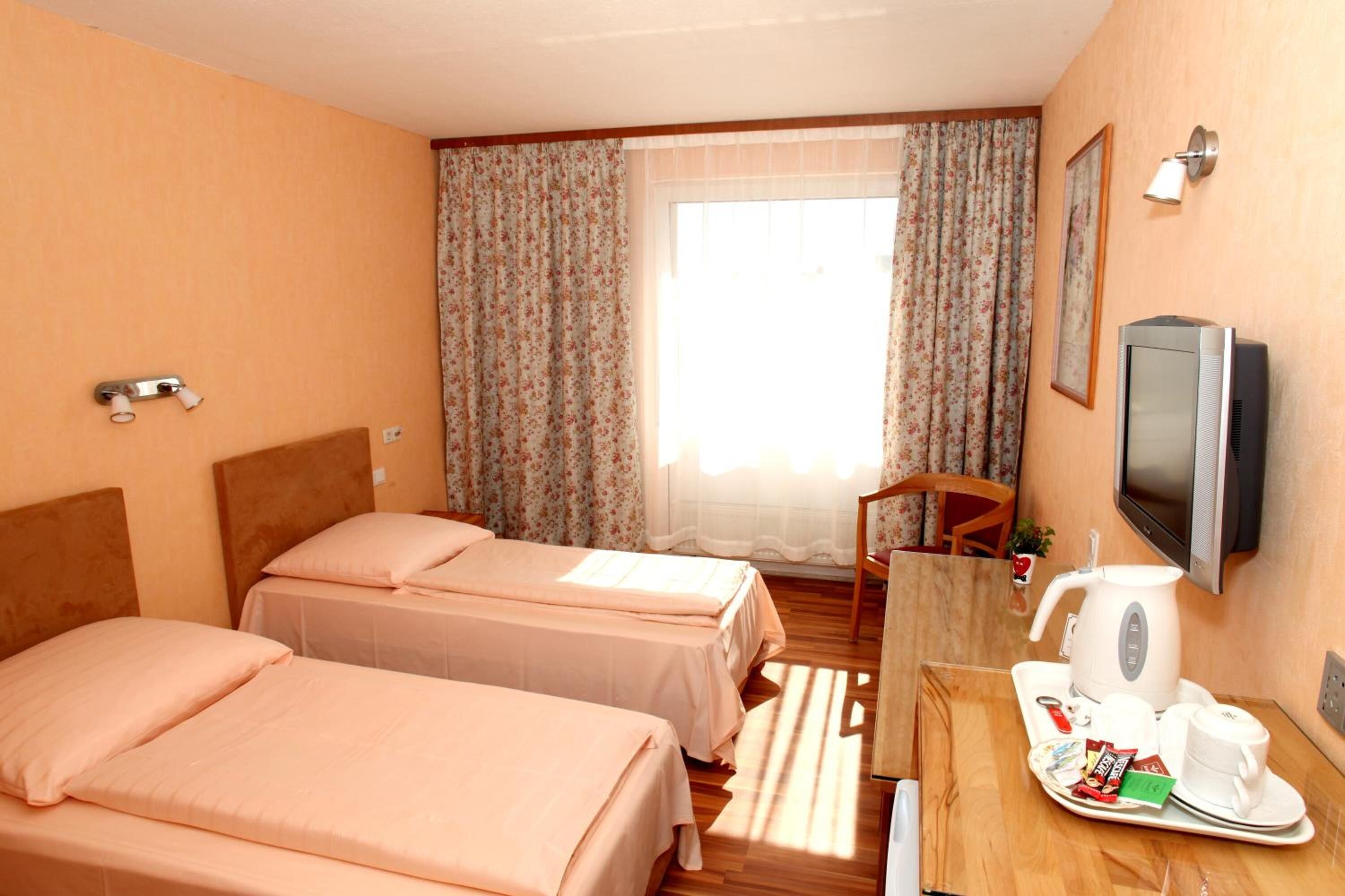 A hotel room with two beds, a wooden desk with a tray of breakfast items, a television, and a window with curtains.