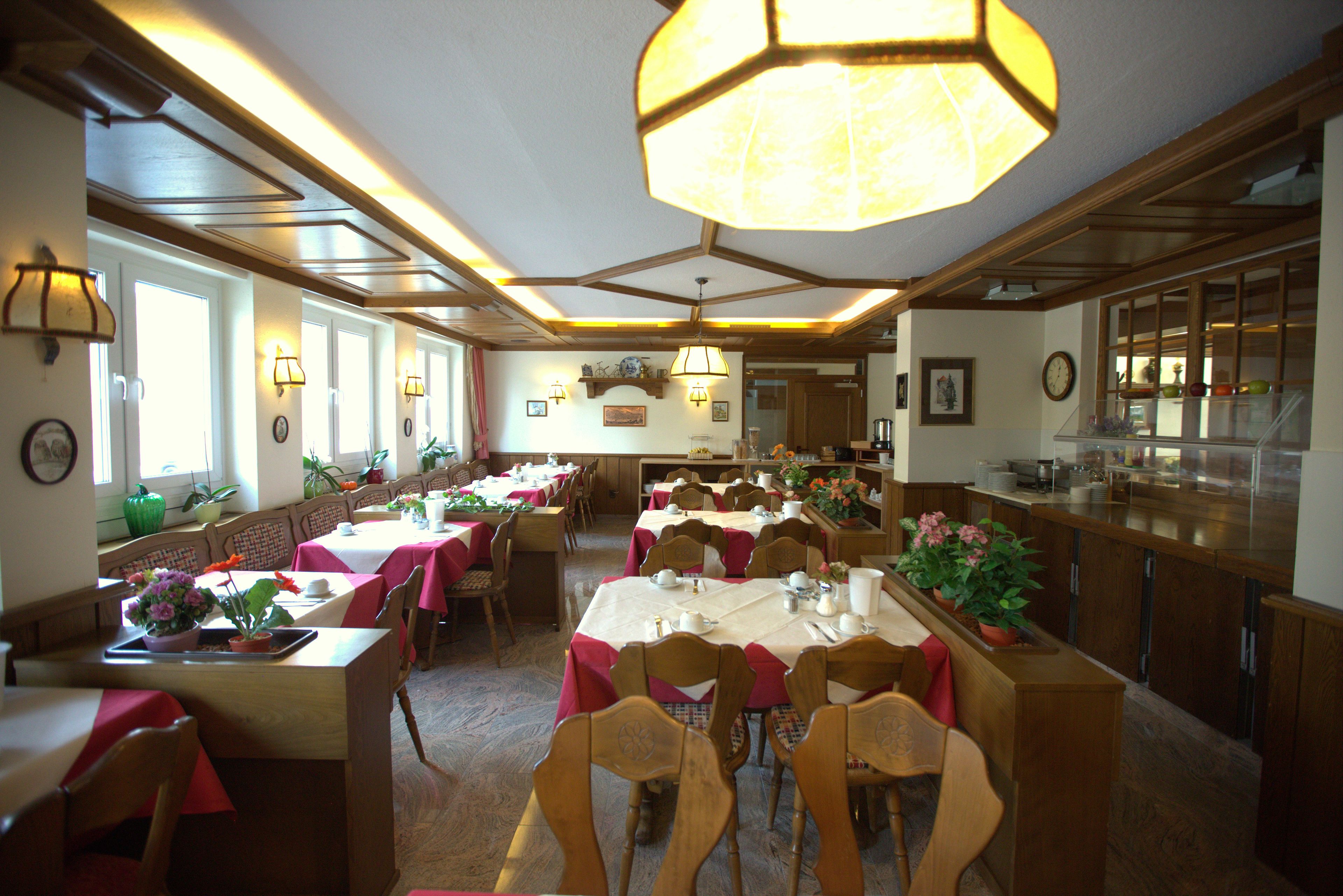 A dining area with multiple tables and chairs, wooden beams on the ceiling, and a large hanging light fixture.