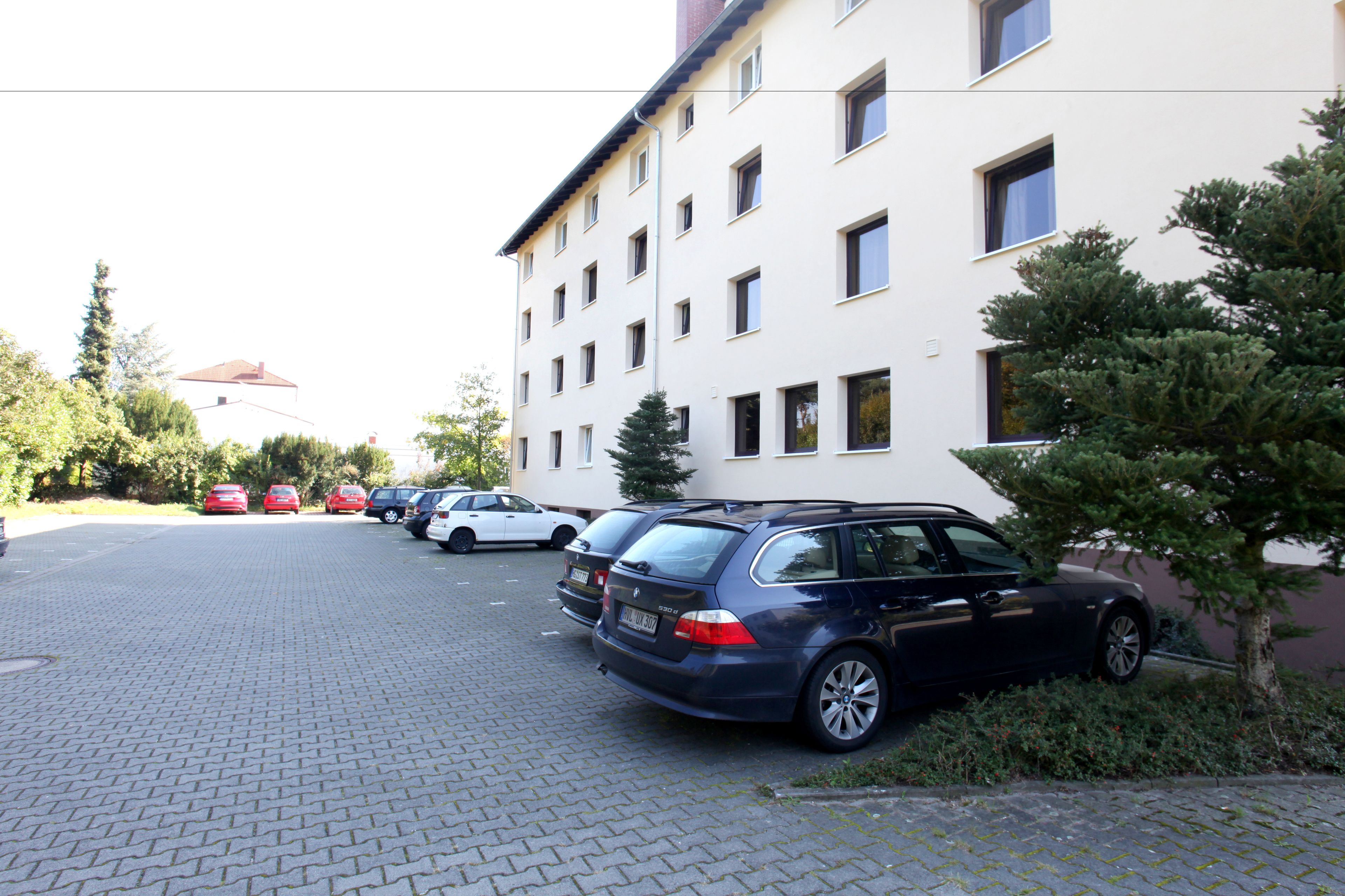 A parking lot with several cars parked in front of a multi-story building with a white facade and multiple windows.