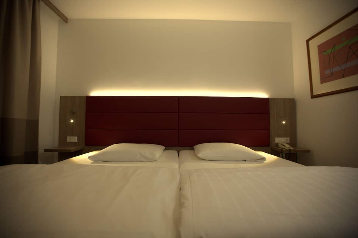 Una cama doble con cabecera roja, dos mesitas de noche y un teléfono en la pared.