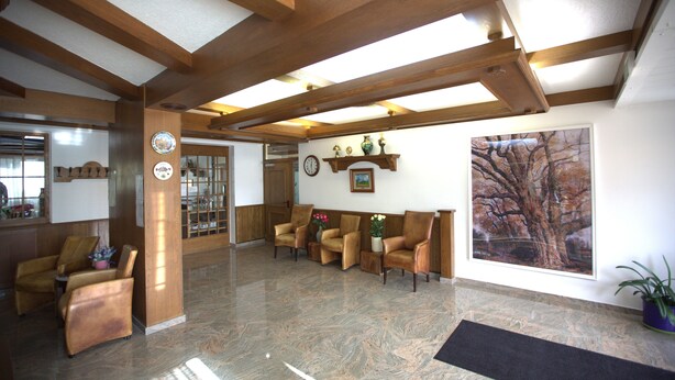 A spacious lobby with wooden beams, a reception desk, several leather armchairs, a large window with a tree view, and a marble floor. - Airport Hotel Walldorf (Moerfelden-Walldorf)