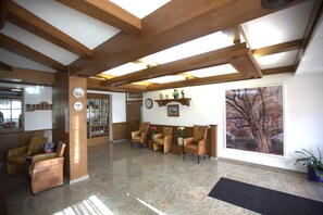 Un vestíbulo espacioso con vigas de madera, un mostrador de recepción, varios sillones de cuero, un gran ventanal con vistas a un árbol y un suelo de mármol.