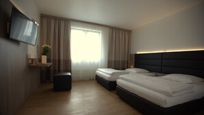 A modern hotel room with a large bed, a TV mounted on the wall, and a bedside table with a vase of flowers. - Airport Hotel Walldorf (Moerfelden-Walldorf)