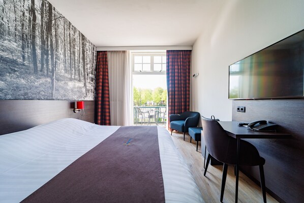 Une chambre d’hôtel dotée d’un grand lit, d’un bureau avec une chaise, d’une télévision et offrant une vue sur un balcon aménagé avec du mobilier d’extérieur.