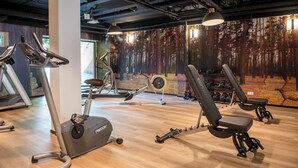 A gym with exercise equipment, a large mural of a forest, and a wooden floor. - Bastion Hotel Apeldoorn Het Loo (Apeldoorn)