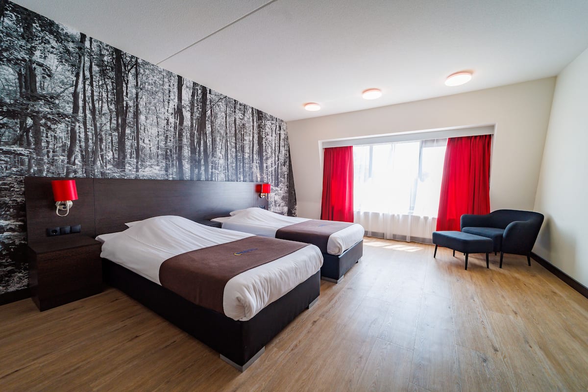 Ein Hotelzimmer mit zwei Betten, einem Nachttisch, einem Sessel und einer großen Wandmalerei zum Thema Wald.