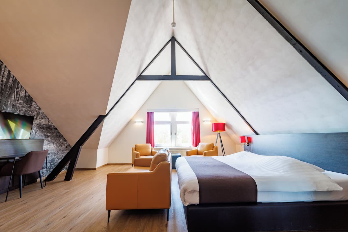 Ein moderner, dreieckiger Raum mit einem Bett, zwei Stühlen, einem Schreibtisch und einer Lampe.