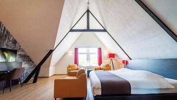 A modern, triangular room with a bed, two chairs, a desk, and a lamp.