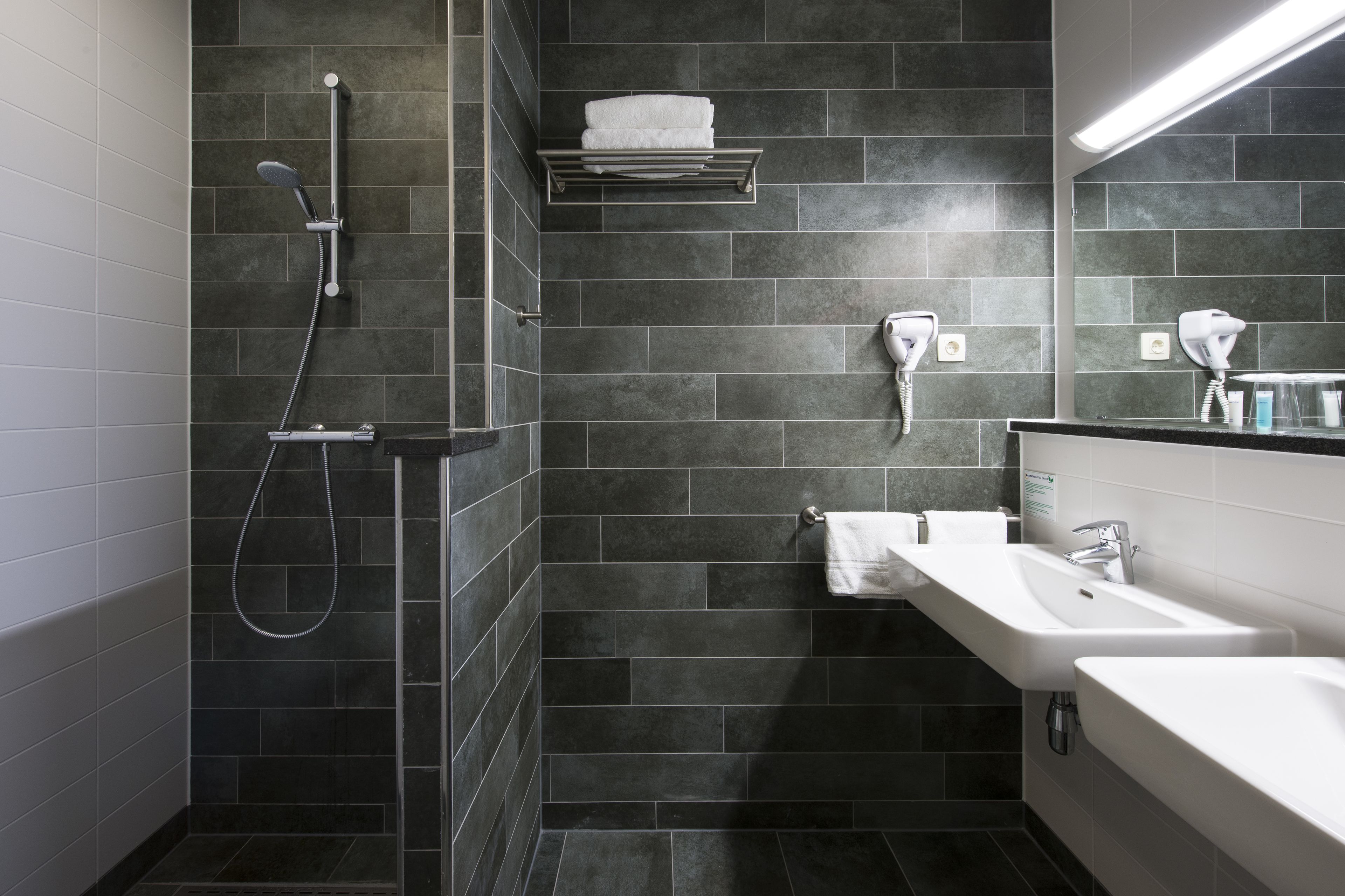Un baño moderno con ducha, dos lavamanos y un perchero para toallas.