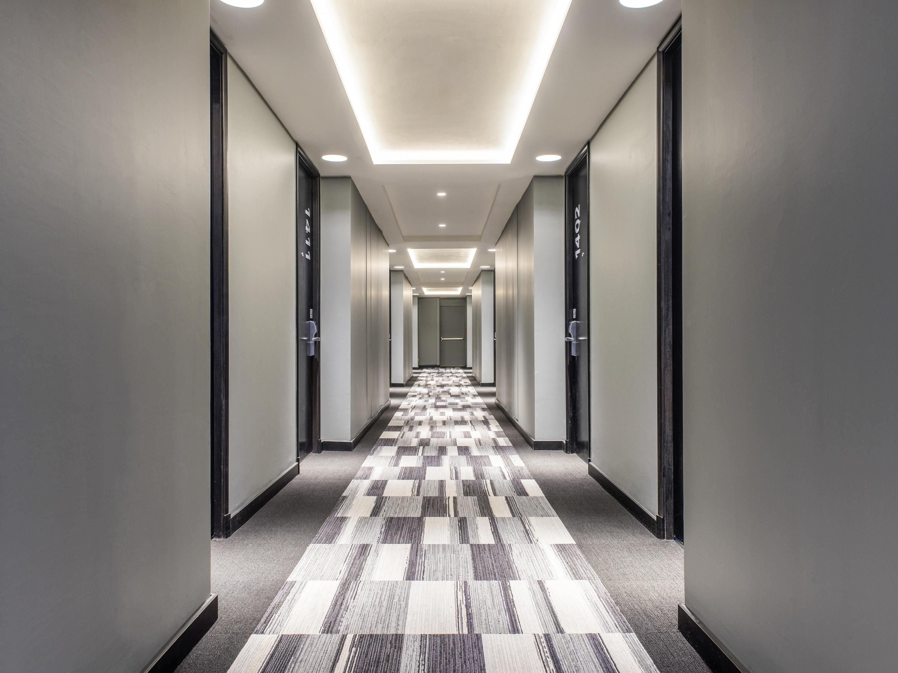 Un pasillo moderno de hotel con alfombra a cuadros, iluminación empotrada y puertas indicadas con números de habitación.