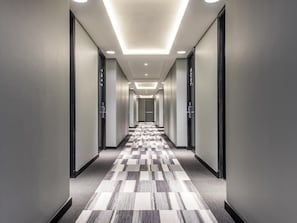Un pasillo moderno de hotel con alfombra a cuadros, iluminación empotrada y puertas indicadas con números de habitación.
