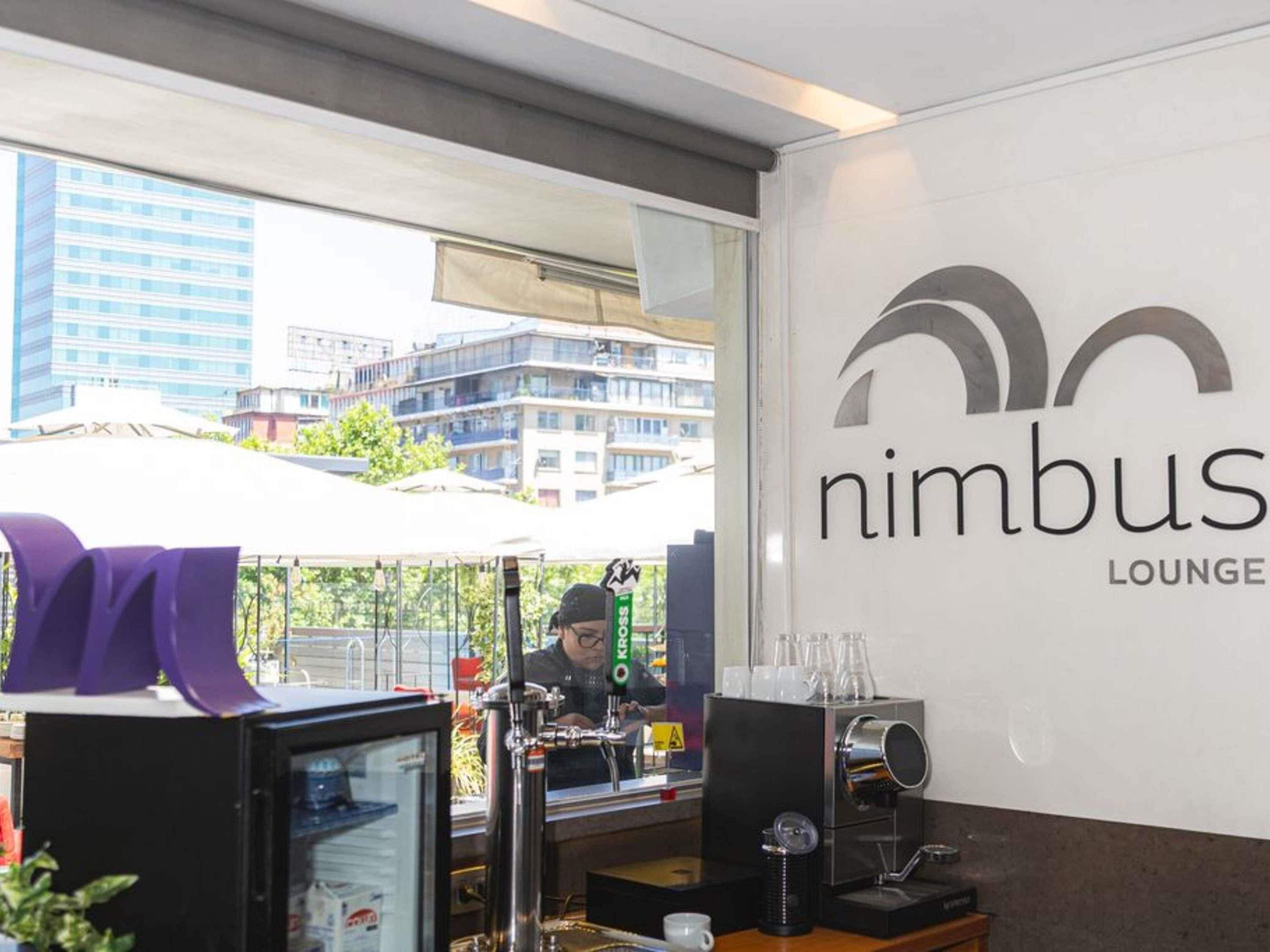 Un bar de café con vistas a edificios, un letrero que dice 'nimbus lounge' y una máquina de café.