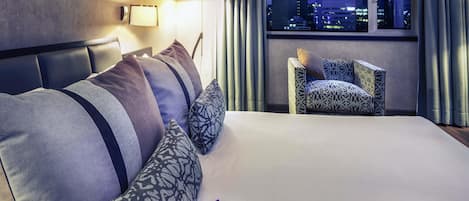 A hotel room with a bed, a chair, and a city view.