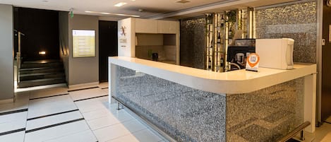 A hotel reception area with a counter, a coffee machine, and a wall-mounted wine rack.
