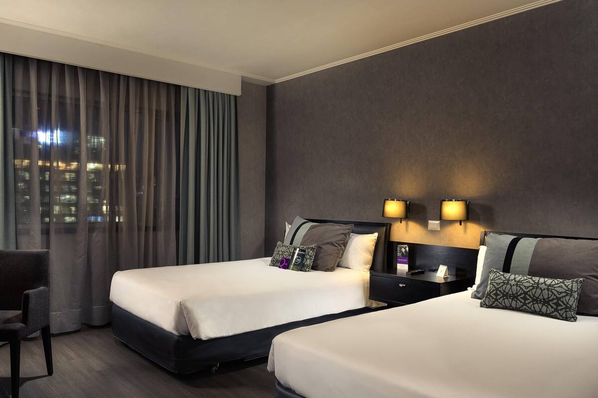 A hotel room with two beds, a desk, and a chair.