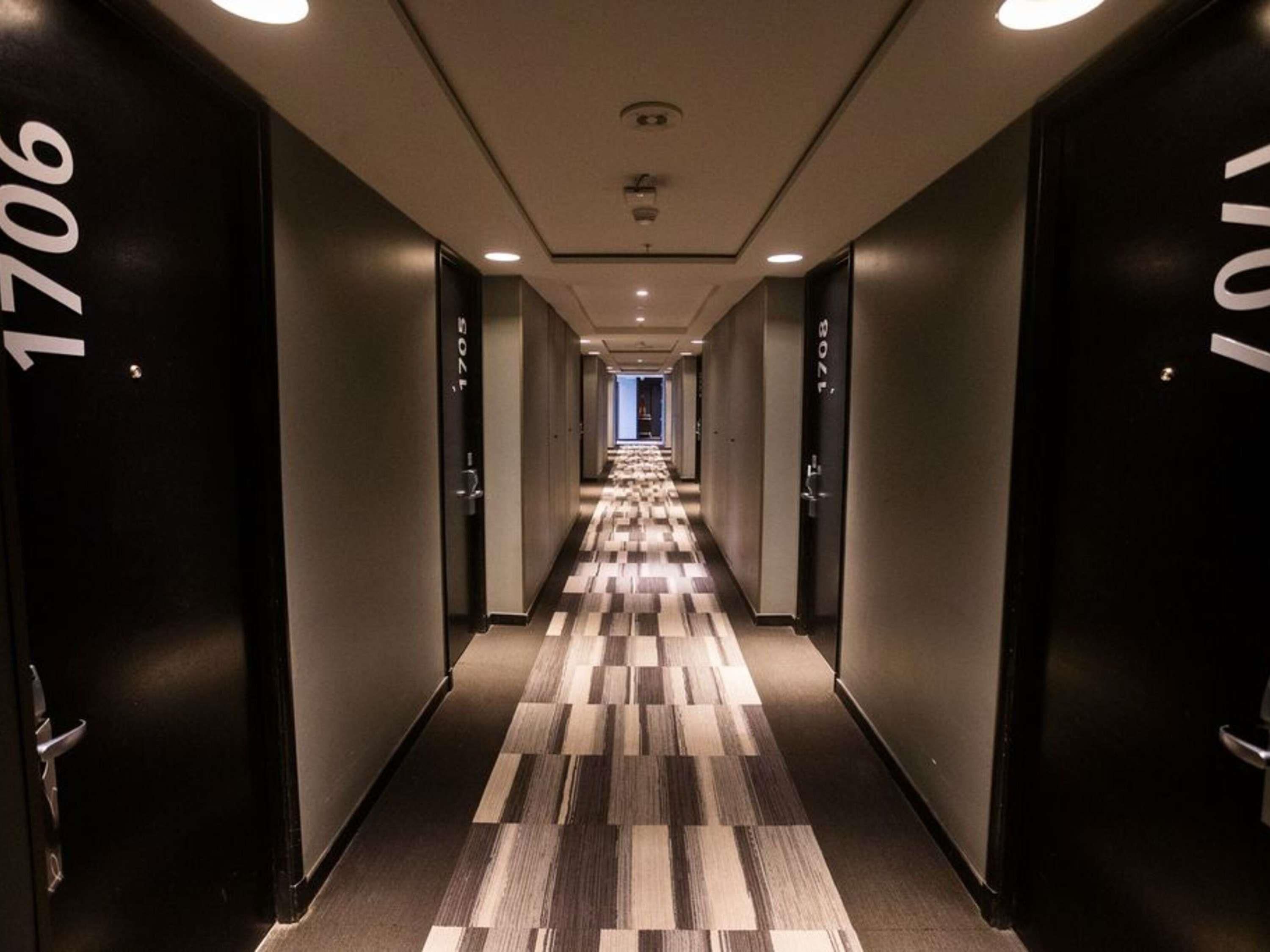 Een hotelgang met donkere muren, genummerde deuren en een kamerbreed tapijt met patroon.
