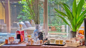 A table with various food items and condiments, a coffee machine, and a vase with dried plants. - Hotel Mec (Milan)