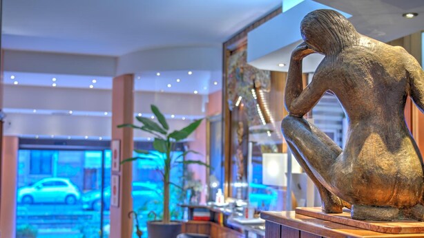 A bronze sculpture of a contemplative figure in a lobby with a view of a street outside. - Hotel Mec (Milan)