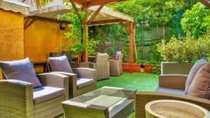 An outdoor patio with wicker furniture and a glass table, surrounded by greenery and a pergola. - Hotel Mec (Milan)