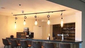Una zona de bar con una barra larga, varios taburetes y lámparas colgantes.